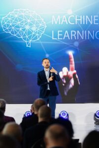 dr Maciej Kawecki na scenie, na ekranie slajd Machine Learning